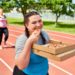 Zwei Frauen joggen über eine Laufstrecke und essen dabei Pizza.