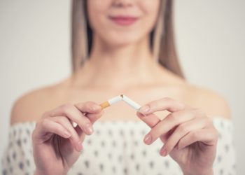 Junge Frau mit fröhlichem Gesichtsausdruck hält eine auseinander gebrochene Zigarette in ihren Händen