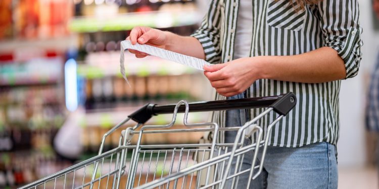 Frau mit Einkaufswagen betrachtet im Supermarkt ihren Einkaufszettel