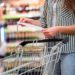 Frau mit Einkaufswagen betrachtet im Supermarkt ihren Einkaufszettel