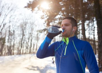 Junger Sportler trinkt Wasser in winterlicher Landschaft