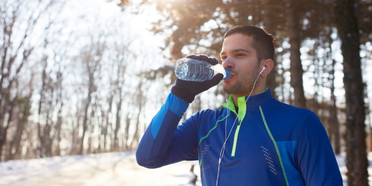 Junger Sportler trinkt Wasser in winterlicher Landschaft