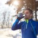 Junger Sportler trinkt Wasser in winterlicher Landschaft