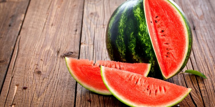 Eine Wassermelone mit zwei herausgeschnittenen Teilen auf einem Holztisch