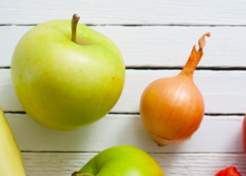 Ein Apfel und eine Zwiebel vor einem weißen Hintergrund.
