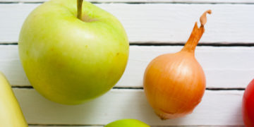 Ein Apfel und eine Zwiebel vor einem weißen Hintergrund.