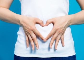 Frau bildet mit ihren Händen ein Herzsymbol vor ihrem Bauch.