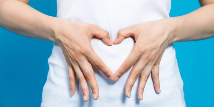 Frau bildet mit ihren Händen ein Herzsymbol vor ihrem Bauch.