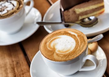 Zwei Tassen Kaffee und ein Stück Torte auf einem Holztisch