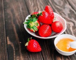 Eine Schale mit Erdbeeren und eine Schale mit Honig auf einem Holztisch