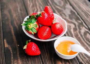 Eine Schale mit Erdbeeren und eine Schale mit Honig auf einem Holztisch