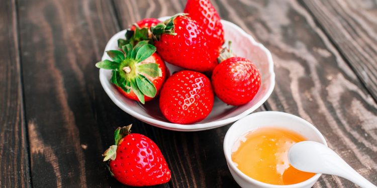 Eine Schale mit Erdbeeren und eine Schale mit Honig auf einem Holztisch