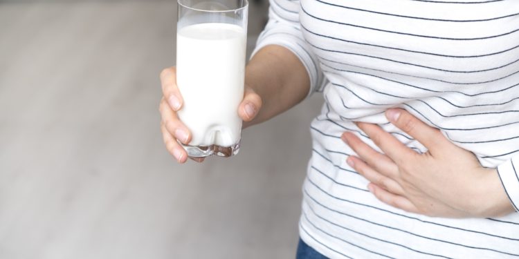 Eine Frau mit einem Glas Milch in der rechten Hand hält sich die linke Hand an den Bauch.