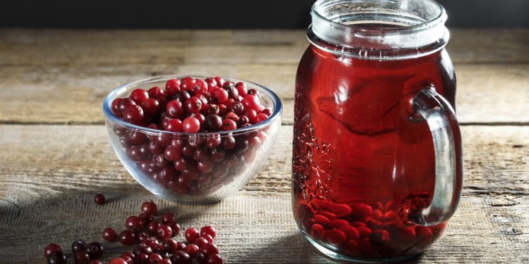 Preiselbeersaft in einem Glaskrug und frische Preiselbeeren auf dem Tisch