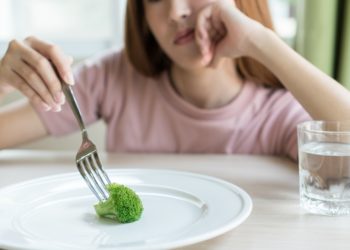 Deprimierte Jugendliche stochert in ein Brokkoliröschen auf einem ansonsten leeren Teller