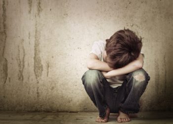 Kleiner Junge in der Hocke legt seinen Kopf in seine verschränkten Arme