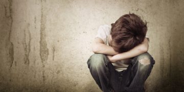 Kleiner Junge in der Hocke legt seinen Kopf in seine verschränkten Arme