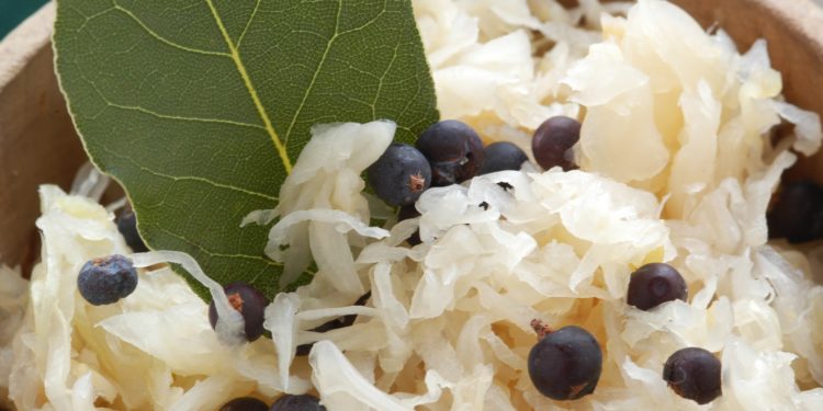 Eine Holzschale mit Sauerkraut, Wacholderbeeren und Lorbeerblatt.