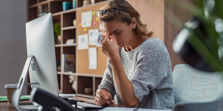 Frau im Büro hat Kopfschmerzen und fasst sich an die Nasenwurzel