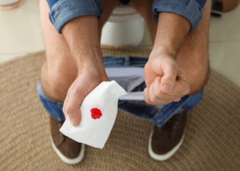 Auf der Toilette sitzender Mann hält Toilettenpapier mit einem Blutfleck