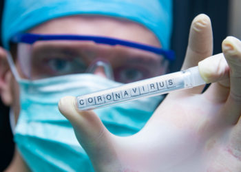 Ein Wissenschaftler hält ein Reagenzglas mit der Aufschrift Coronavirus in der Hand