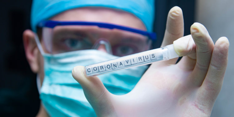 Ein Wissenschaftler hält ein Reagenzglas mit der Aufschrift Coronavirus in der Hand