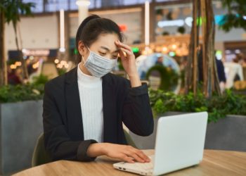 Eine Frau sitzt mit einem Mundschutz vor einem Notebook.