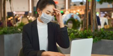 Eine Frau sitzt mit einem Mundschutz vor einem Notebook.