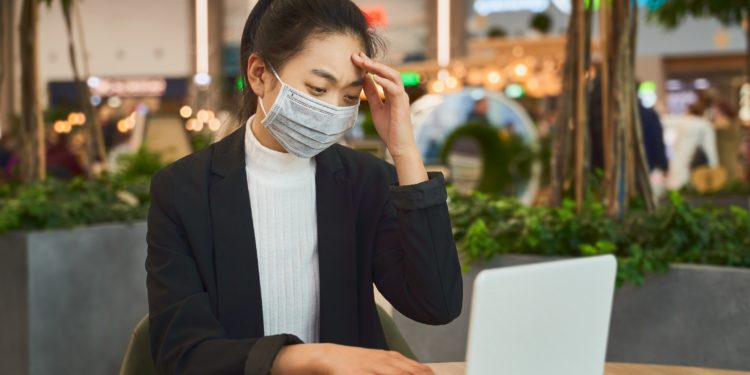 Een vrouw zit met een gezichtsmasker voor een notitieboekje.