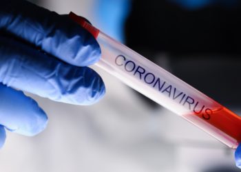 Männliche Hand in blauen Handschuhen hält eine mit Blut gefüllte Ampulle mit der Aufschrift Coronavirus
