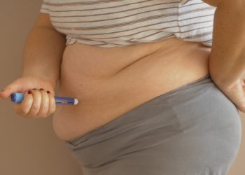 Eine übergewichtige Frau setzt sich eine Insulinspritze in den Bauch.