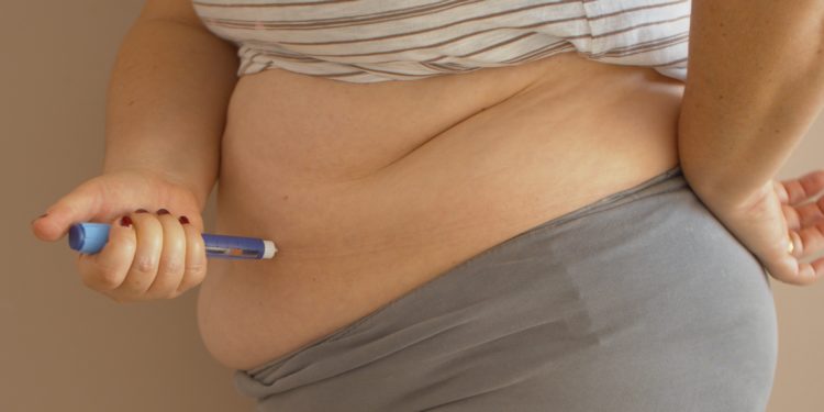 Eine übergewichtige Frau setzt sich eine Insulinspritze in den Bauch.