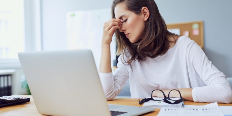 Gestresste junge Frau im Büro fasst sich mit einer Hand in das Gesicht