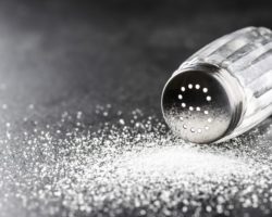 Salzstreuer und verschüttetes Salz auf einer schwarzen Oberfläche