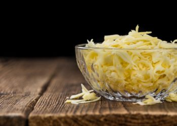 Glasschüssel mit geriebenem Käse auf einem Holztisch