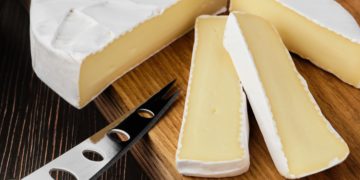 Ein angeschnittener Camembert auf einem Holzbrett mit Käsemesser
