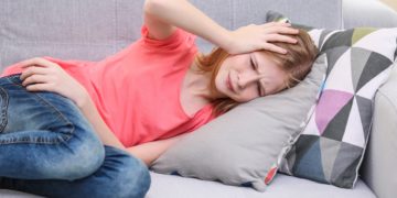 Junge Mädchen liegt mit Kopfschmerzen auf dem Sofa