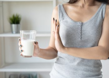 Eine Frau hält ein Glas mit Milch in der rechten Hand, die linke Hand macht eine abwehrende Geste.