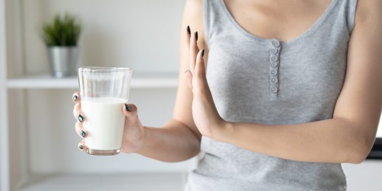 Eine Frau hält ein Glas mit Milch in der rechten Hand, die linke Hand macht eine abwehrende Geste.