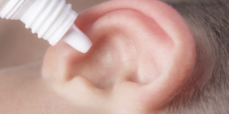 Medizinische Pipette mit Ohrentropfen über dem Ohr eines Kindes