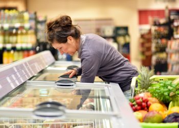 Frau holt Ware aus einer Tiefkühltheke im Supermarkt