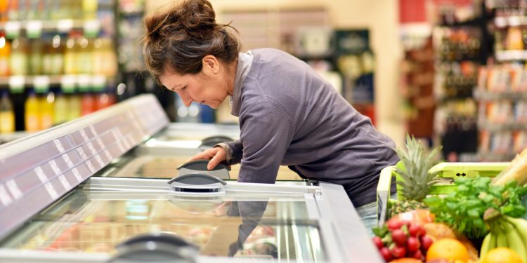 Frau holt Ware aus einer Tiefkühltheke im Supermarkt