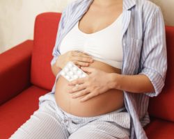 Eine schwangere Frau hält eine Packung mit Tabletten in der Hand.