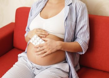 Eine schwangere Frau hält eine Packung mit Tabletten in der Hand.