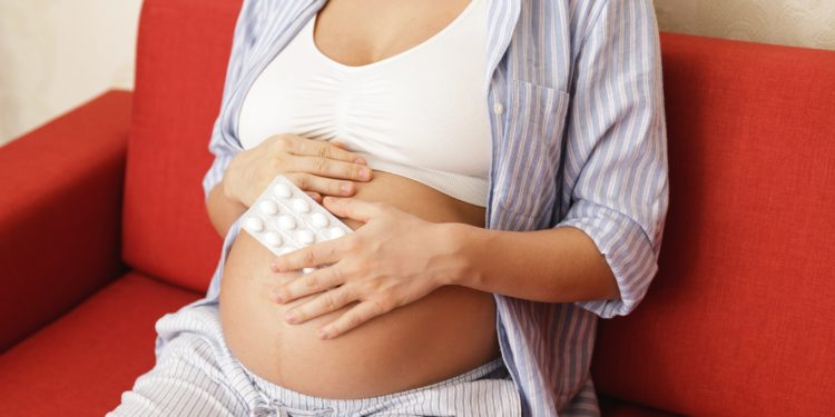 Eine schwangere Frau hält eine Packung mit Tabletten in der Hand.