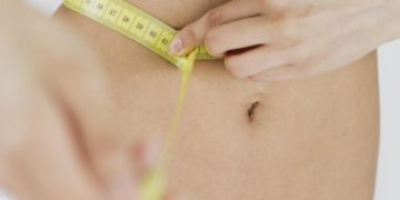 Ein schlanker Bauch, der von einem Maßband umsäumt ist.