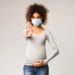Eine Schwangere trägt eine Atemschutzmaske und macht eine abwehrende Geste.
