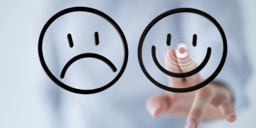 Ein trauriger und ein fröhlicher schwarzer Smiley und eine Hand, die mit Zeigefinger und MIttelfinger auf den fröhlichen Smiley zeigt