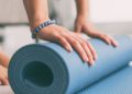 Frau rollt eine Fitnessmatte in der Wohnung aus