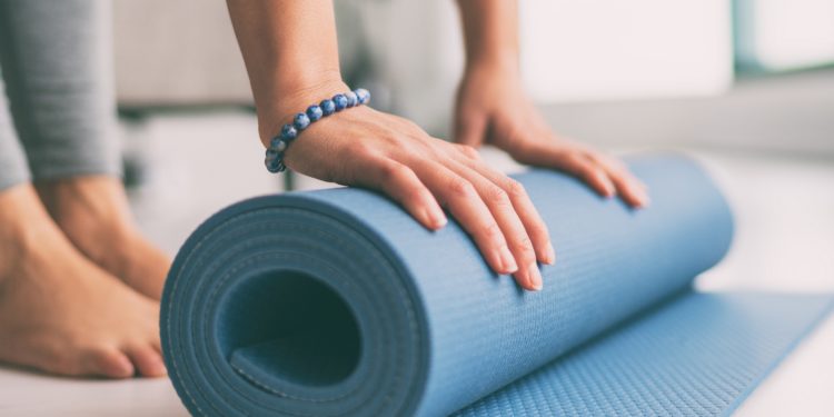 Frau rollt eine Fitnessmatte in der Wohnung aus